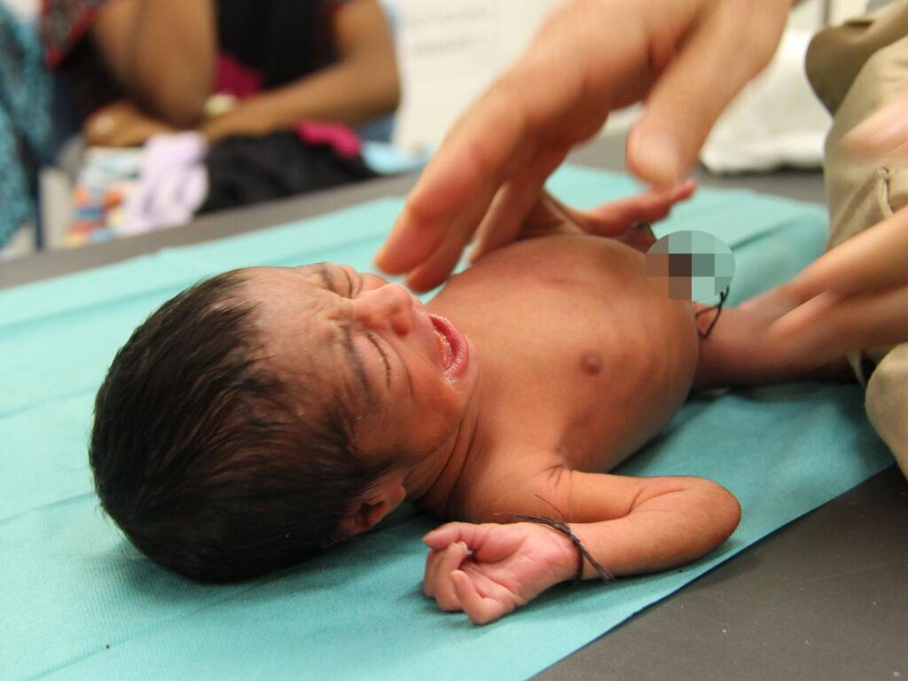 Newborn baby crying on a hospital bed.